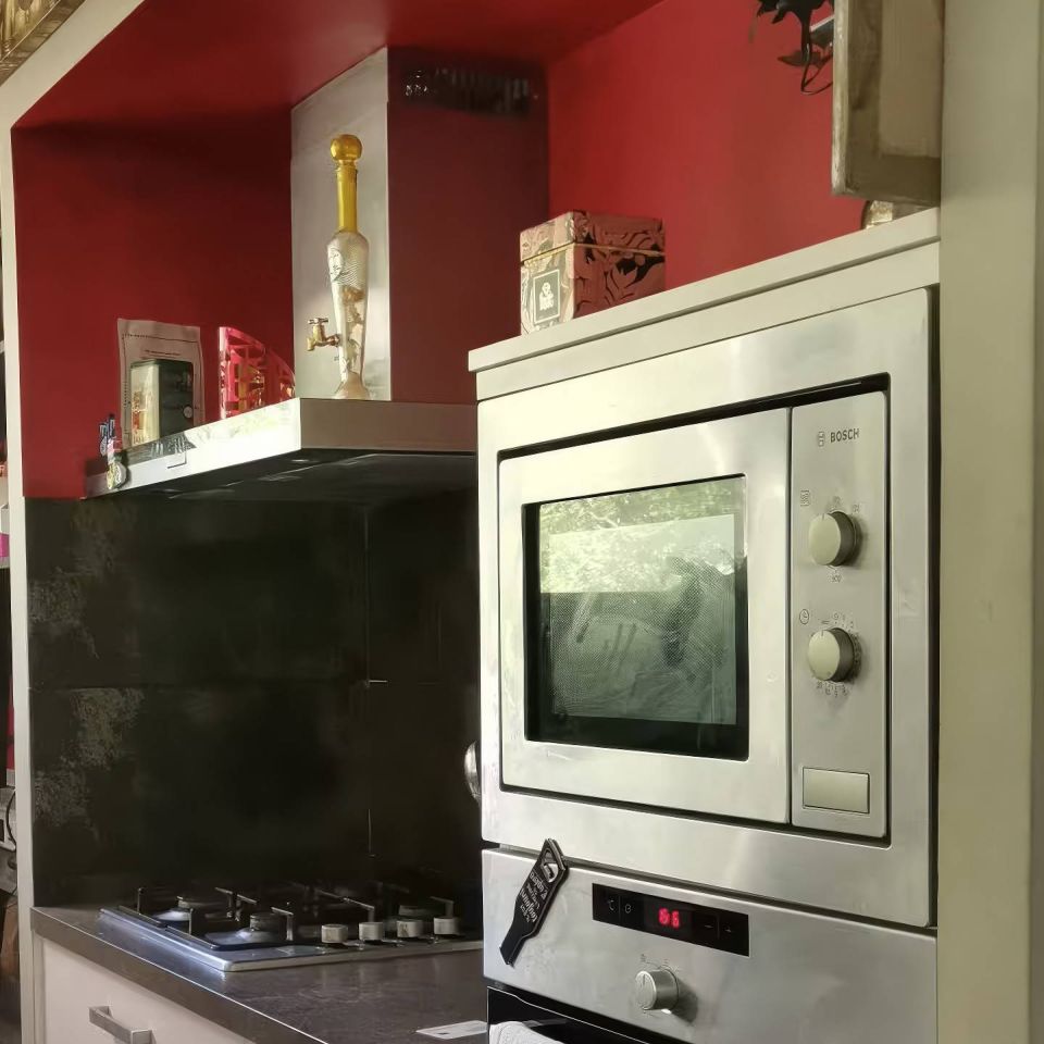 Cuisine moderne avec des accents rouges, four en acier inoxydable et cuisinière à gaz ; serviettes accrochées, œuvres d'art au mur.