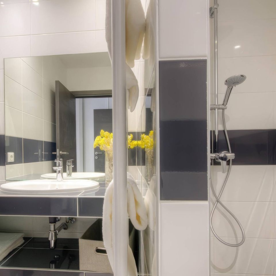 A modern bathroom features a shower, sink, mirror, and decorative yellow flowers. Clean, sleek design with towels.