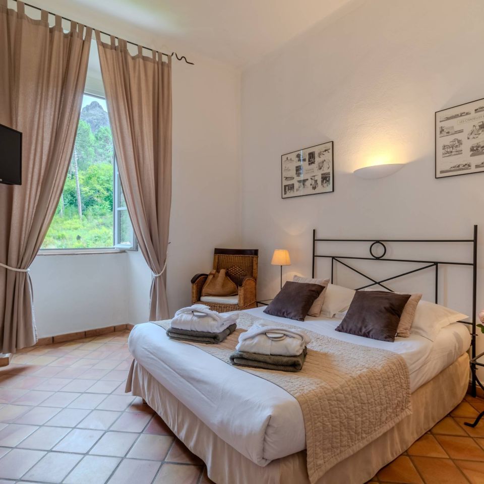 Cosy bedroom with a double bed, TV, soft lighting, and a view of greenery outside. Elegant decor touches.