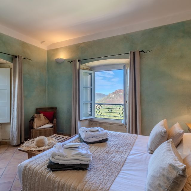 Gemütliches Schlafzimmer mit hellgrünen Wänden, großen Fenstern und Blick auf die Berge, ausgestattet mit einem bequemen Bett und sanfter Dekoration.