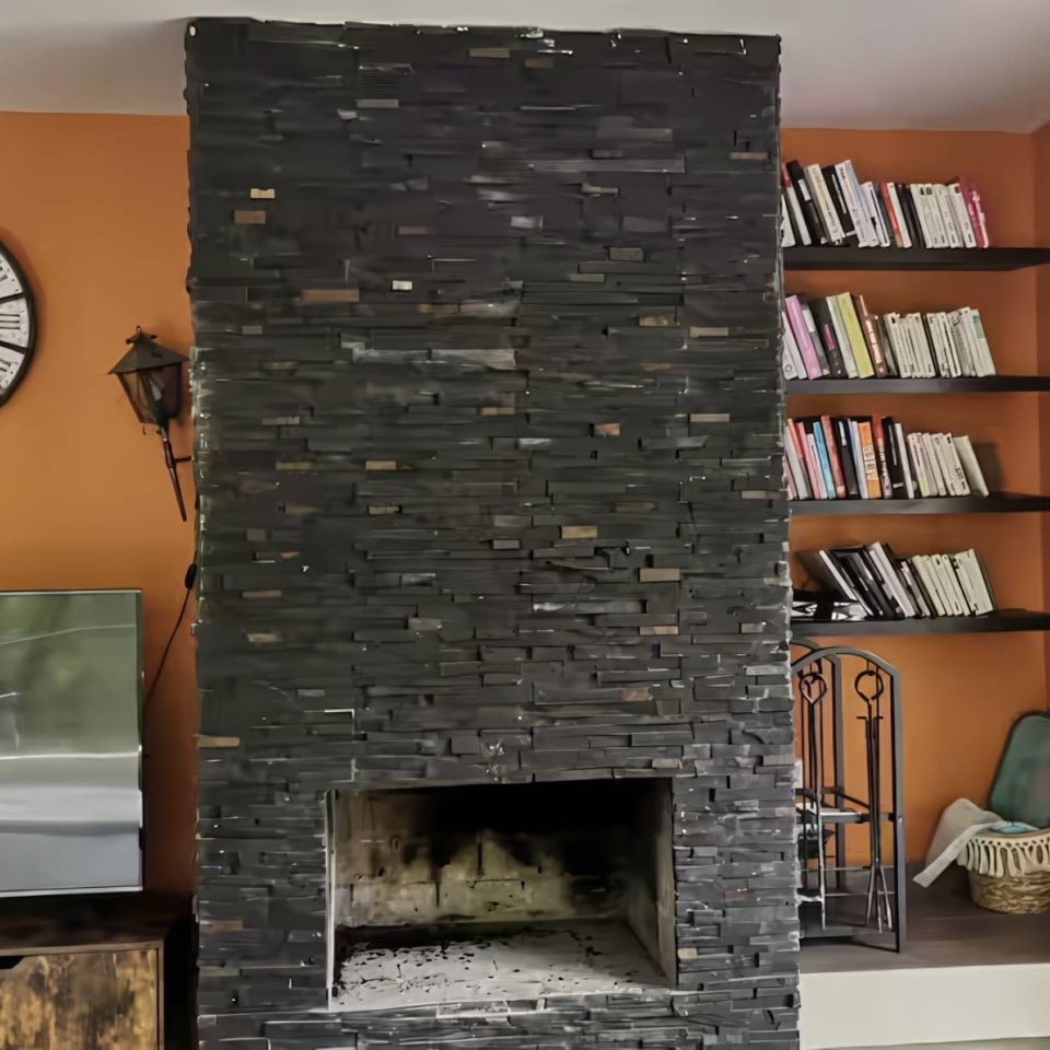 Espace de vie moderne avec une cheminée en pierre noire, des étagères, une grande horloge et des murs orange chaleureux.