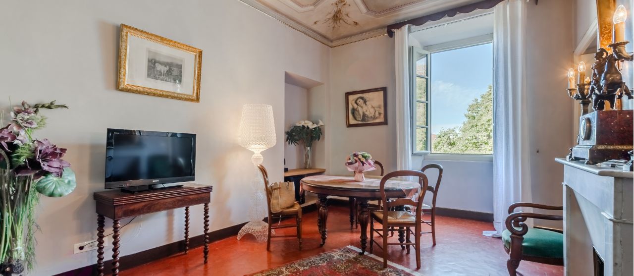 A charming lounge with a vintage feel, featuring a TV, elegant decor, and a window view of greenery.