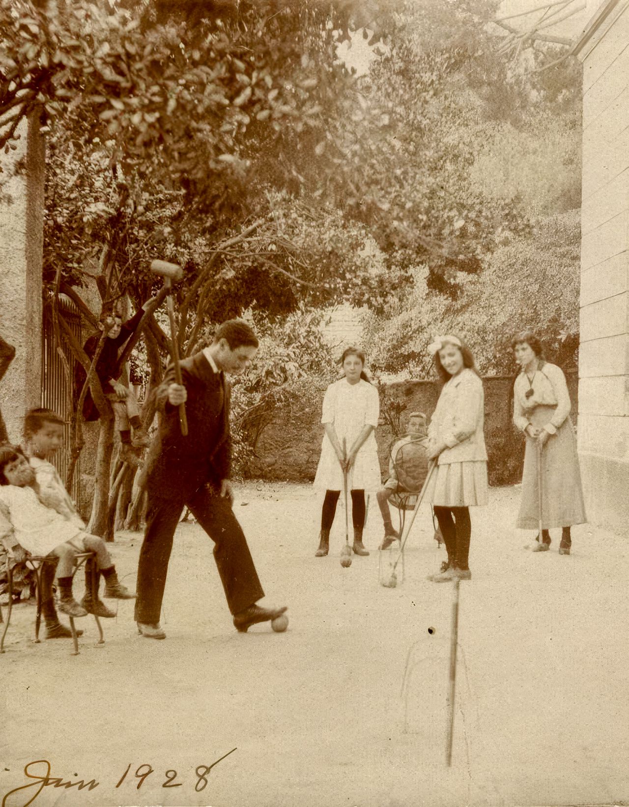 A sepia-toned photo from 1928 shows children and adults playing croquet in a garden.