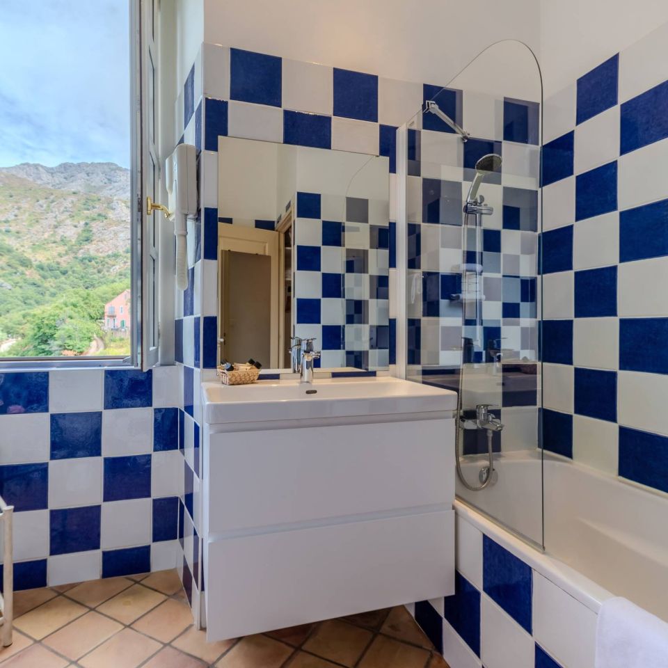 A stylish bathroom features blue and white tiled walls and a view of the mountains through an open window.