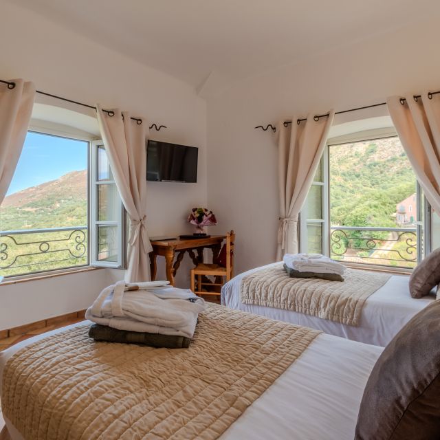 Bright room with two beds, large windows, mountain views, a TV, and a wooden table. Cozy and inviting atmosphere.