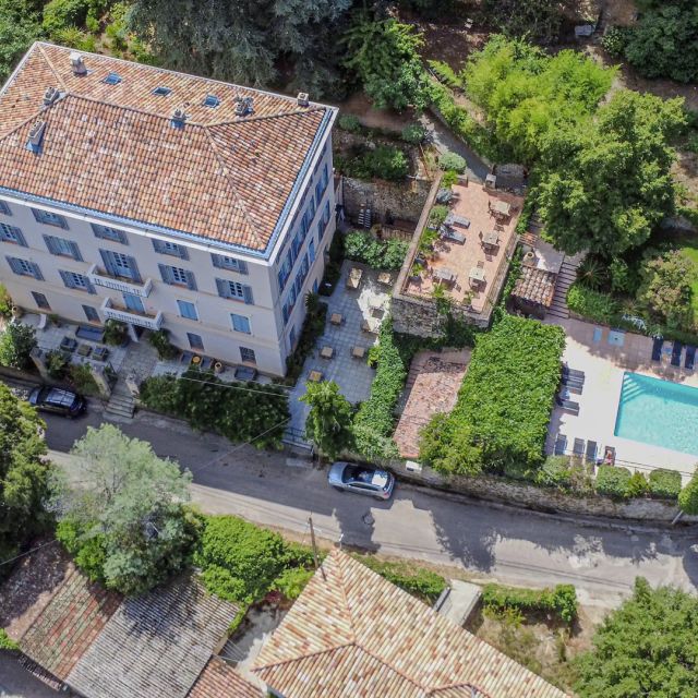 Aerial view of a stylish hotel with a pool surrounded by greenery and residential areas. Sunlit and inviting.