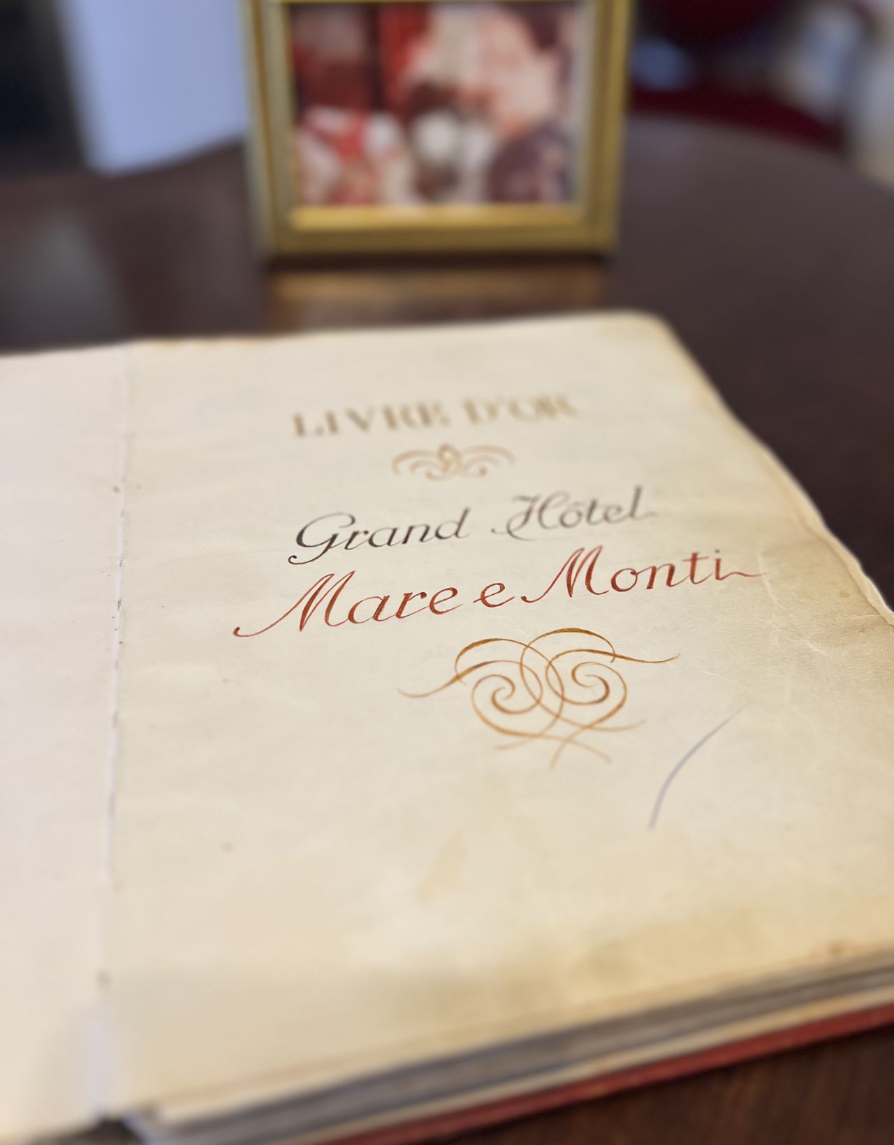 Ein offenes Buch mit dem Titel "Livre d'Or" vom Grand Hotel Mare e Monti, mit einem gerahmten Foto im Hintergrund.