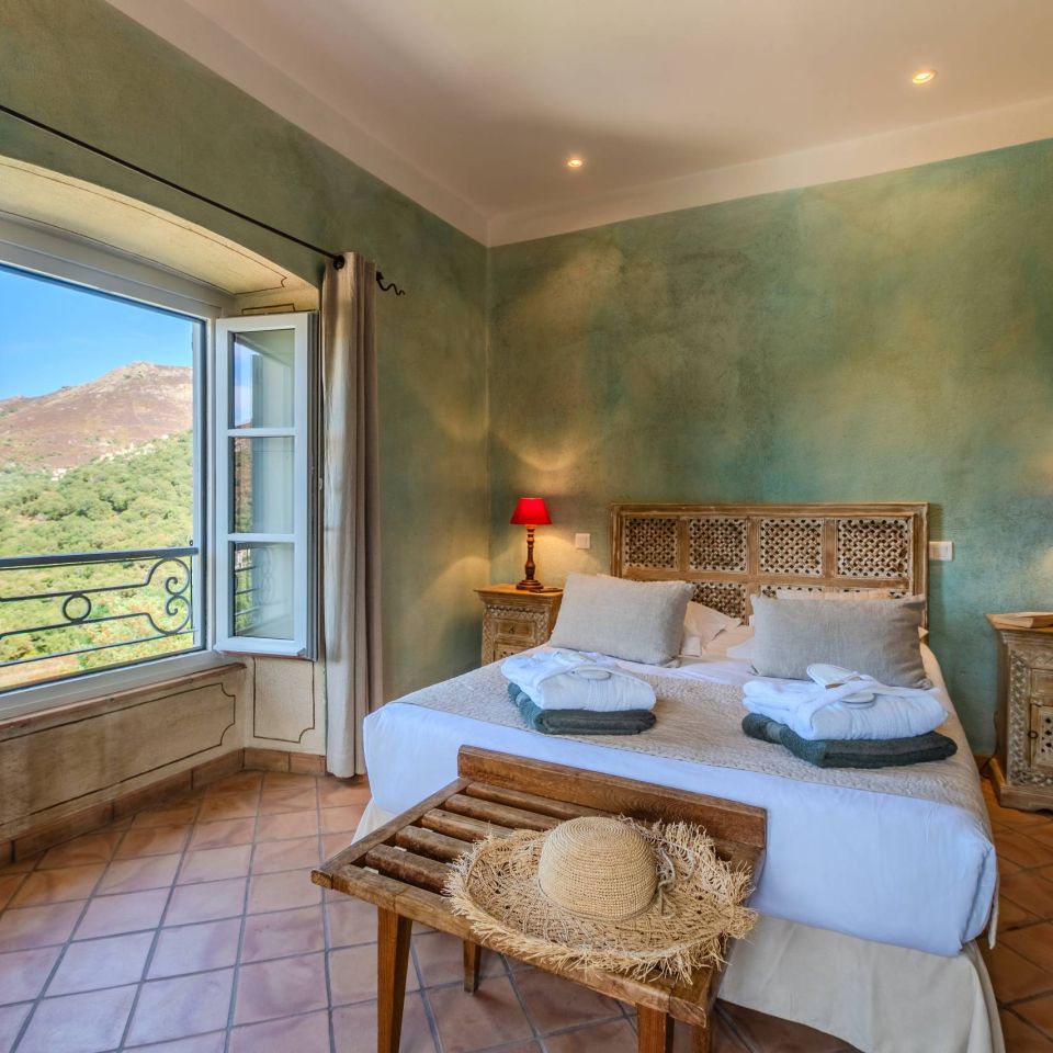 Camera accogliente con pareti verdi, vista sulle montagne, mobili in legno e illuminazione soffusa. Atmosfera serena e invitante.