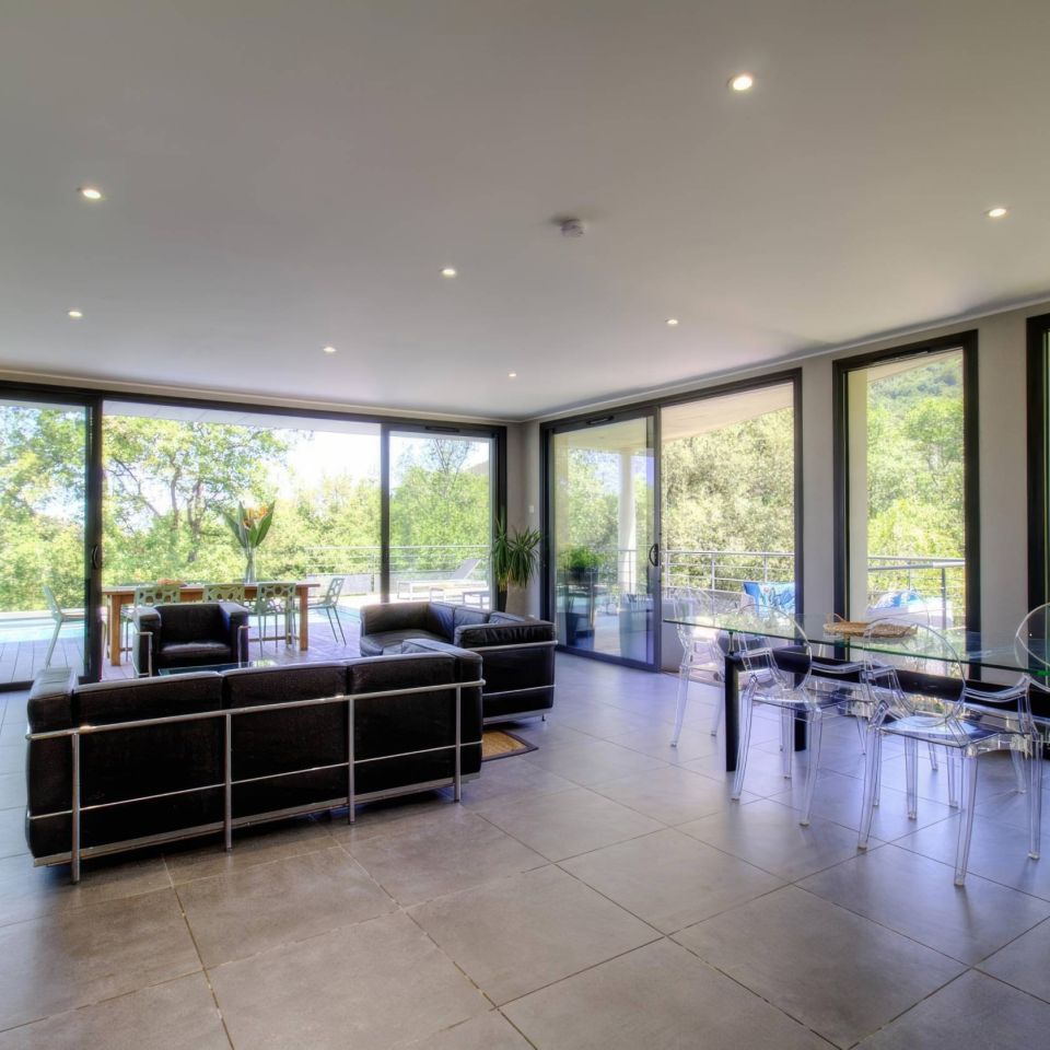 Modern living room with large windows, sleek furniture, and a view of lush greenery outside.