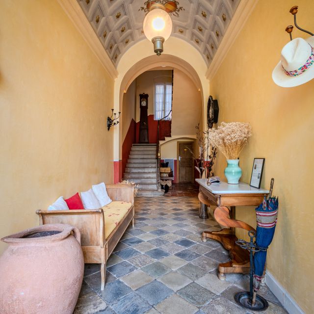 A cosy hallway features a staircase, patterned floor, a bench, decor, and natural light. Warm and inviting ambiance.