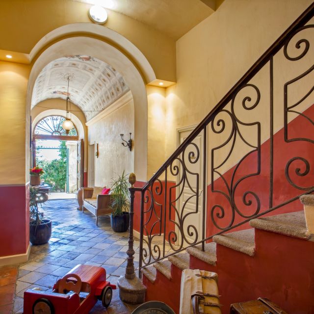 Un couloir présente une rampe d'escalier décorative, des murs colorés et une entrée accueillante agrémentée de plantes en pot.