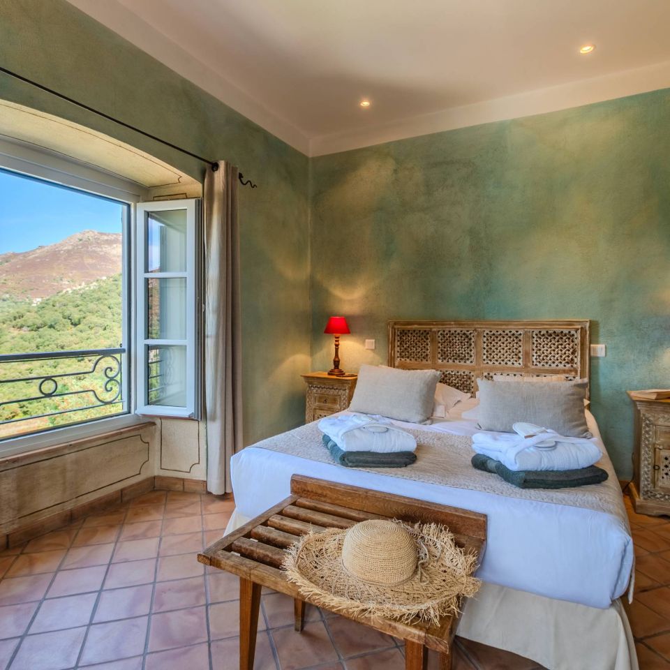 Cozy bedroom with green walls, a view of the mountains, wooden furnishings, and soft lighting. Serene and inviting atmosphere.