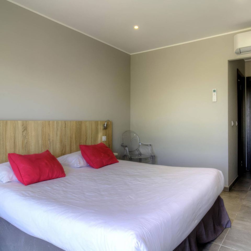 A modern room with a double bed, pink cushions, a minimalist design, and an air conditioning unit.