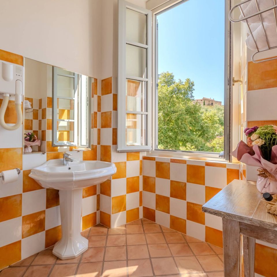 Bright bathroom with orange and white tiles, a sink, and a window showcasing greenery outside. Cozy and inviting.