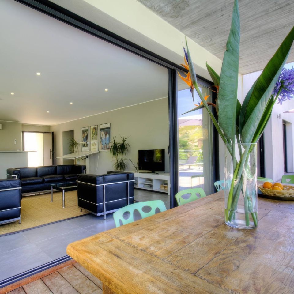 Modern living space with sleek furniture, greenery, and a view of an outdoor area through large glass doors.