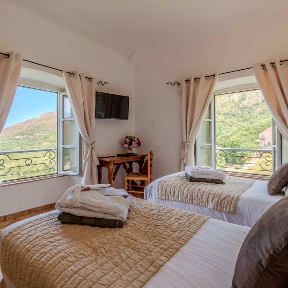 A cosy bedroom featuring two beds, large windows with scenic views, and a small table. Bright and inviting atmosphere.