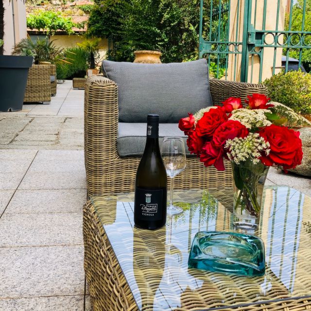 Una scena accogliente nel patio con un tavolo in vimini, vino, un bicchiere e un vivace mazzo di rose rosse. Verdeggiante sullo sfondo.