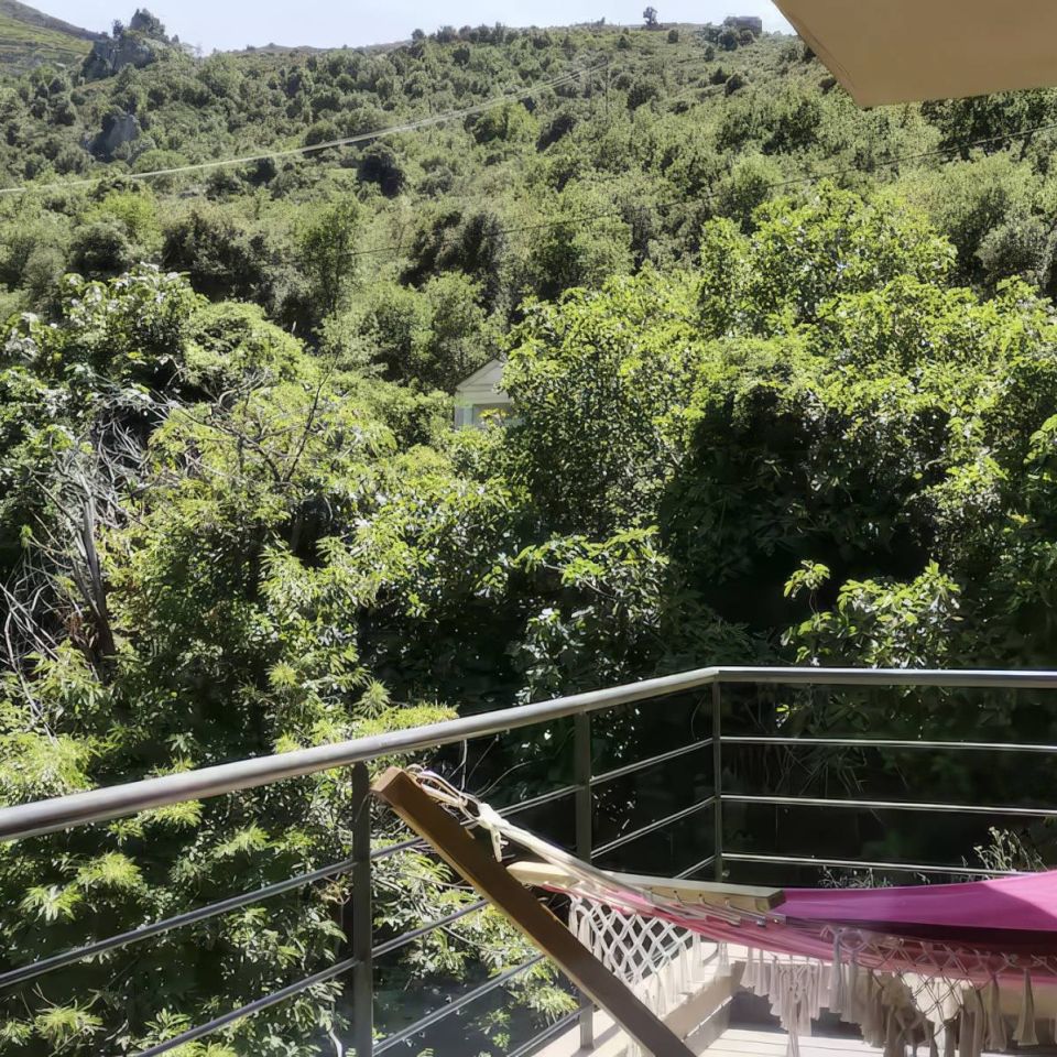 A sunny balcony overlooking lush green hills and trees, featuring a cosy hammock for relaxation.