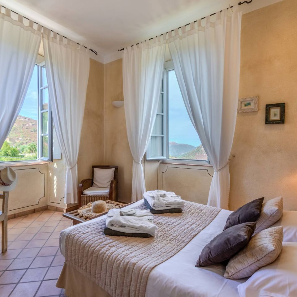 Bright, serene bedroom with a cosy bed, large windows, and soft curtains, showcasing scenic views and refined décor.