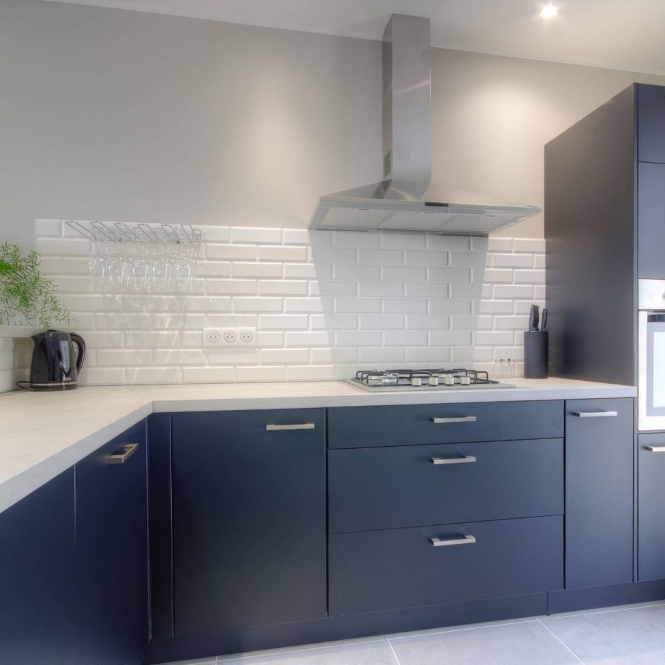 Modern kitchen with dark cabinetry, stainless steel appliances, a white tile backsplash, and a green plant for decoration.
