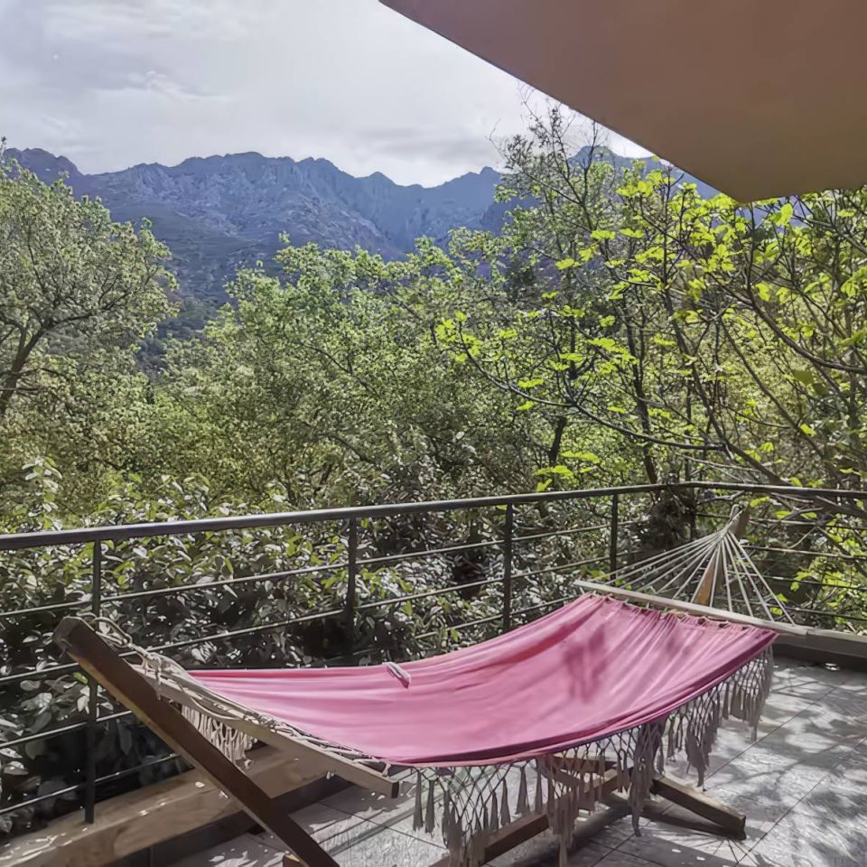 A cosy balcony with a pink hammock overlooks lush greenery and distant mountains under a bright sky.