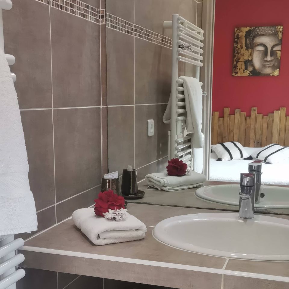A stylish bathroom featuring a sink, towels, decor, and a mirror reflecting a cosy room with a red wall.