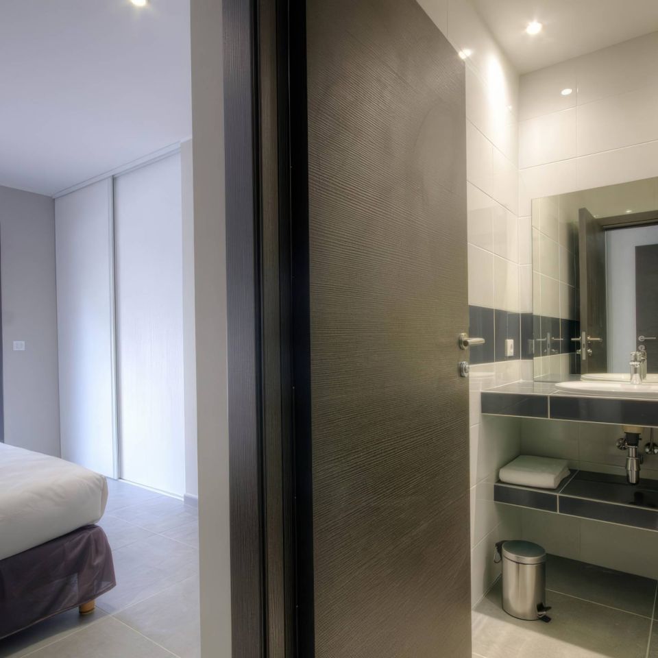 Modern bedroom with large window, connecting to a stylish bathroom featuring a mirror and floral decor.