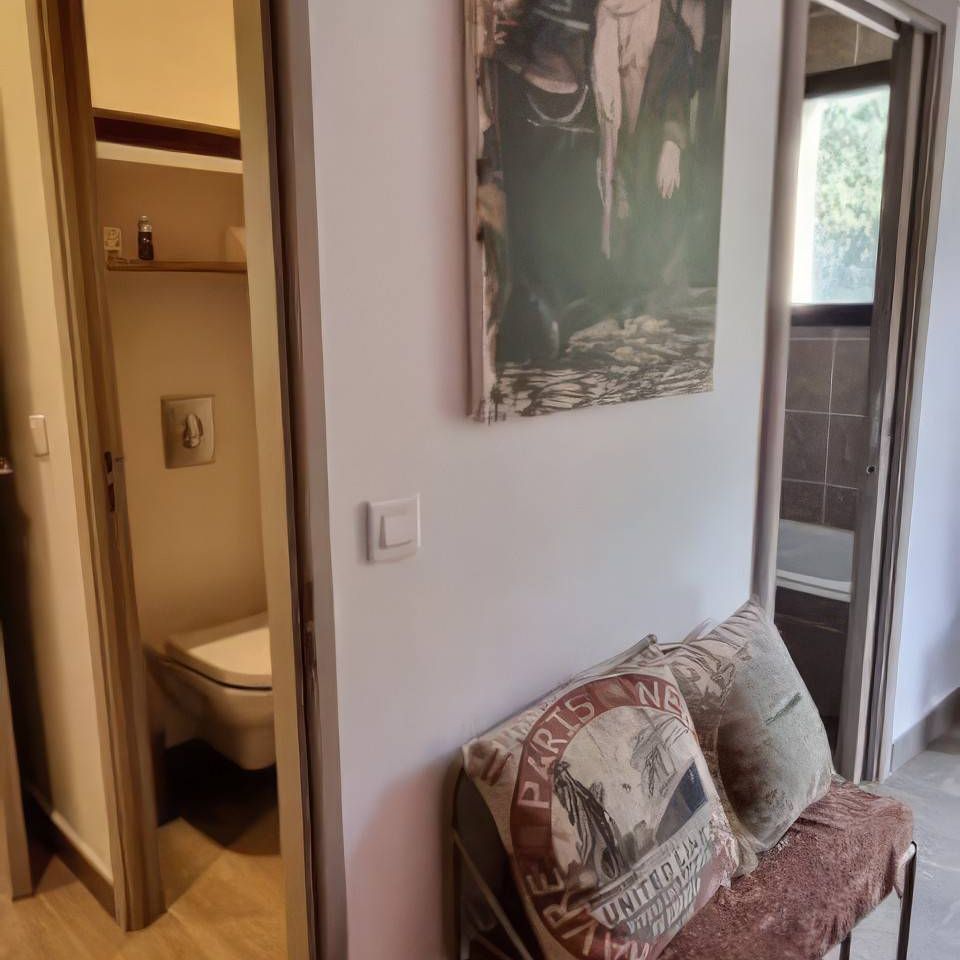 A small hallway features a vintage photograph, a decorative bench with cushions, and doors to a bathroom and another room.