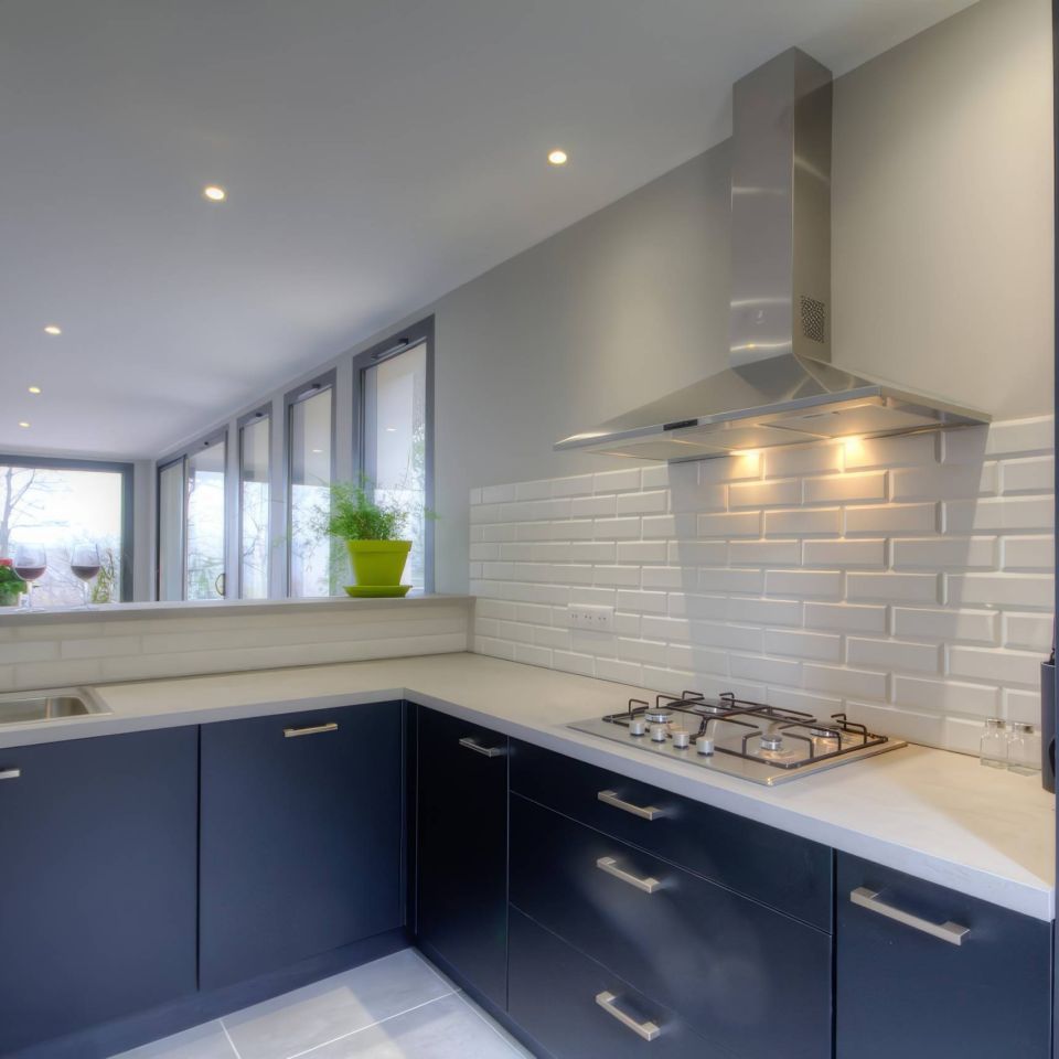 Modern kitchen with dark cabinetry, stainless steel appliances, and large windows offering natural light.