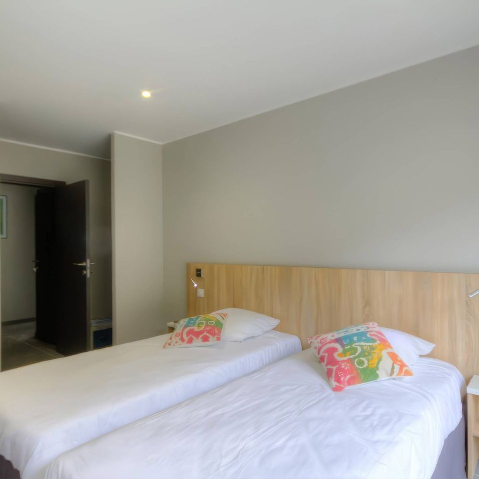 A modern, minimalist charming hotel room with two beds, colourful pillows, and a neutral colour scheme.