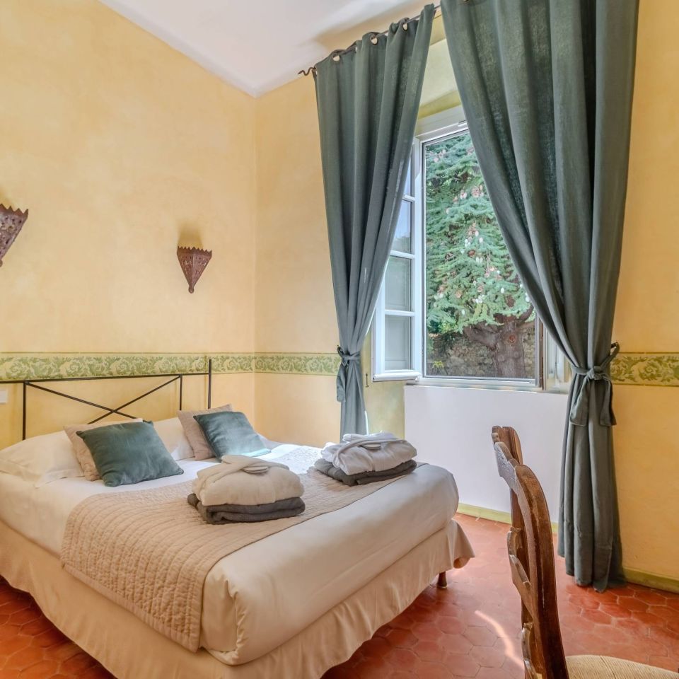 Bright, cozy bedroom with yellow walls, a double bed, elegant curtains, and a charming window view.