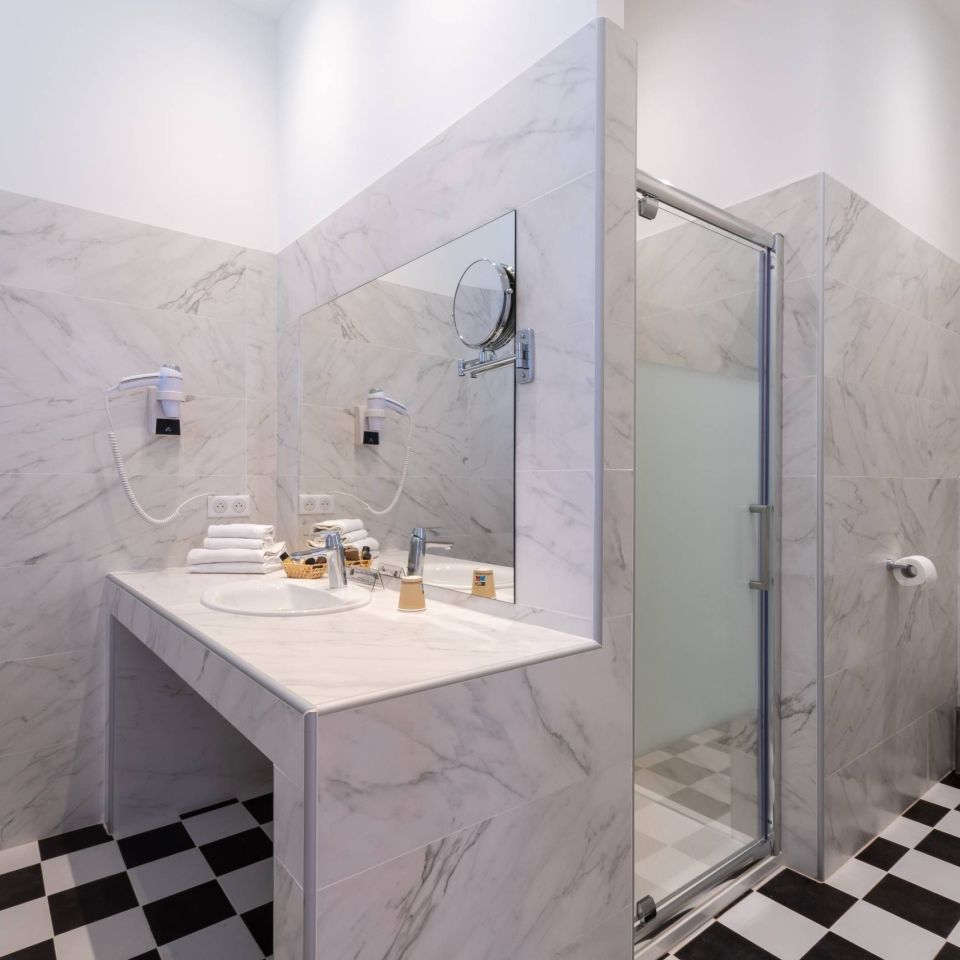 Modern bathroom featuring marble walls, a shower, a sink with towels, and a checkered floor. Clean and stylish design.
