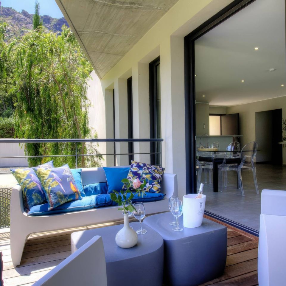 Modern balcony with colourful cushions, plants, and a dining area visible indoors. Relaxing outdoor space.