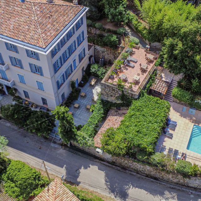 Vista aerea di un grande edificio con una piscina e un'area salotto all'aperto, circondato da una lussureggiante vegetazione.